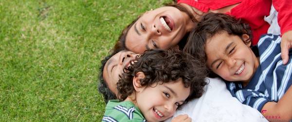 2 children and mother laughing and smiling piled on top of dad on the grass